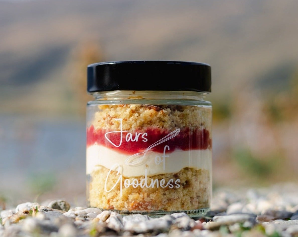 Glass jar with layers of lemon cake, frosting and raspberry coulis