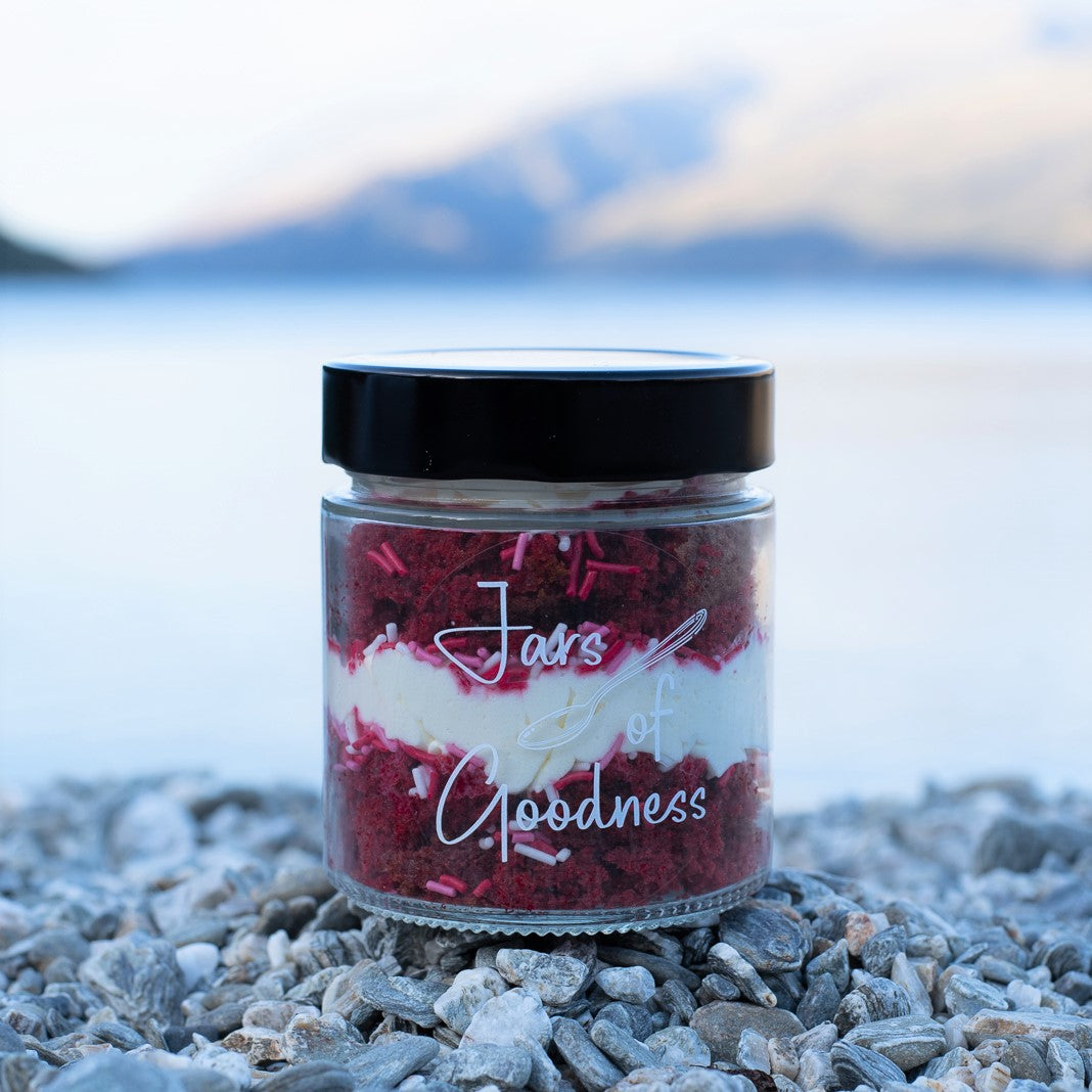 layers of red velvet cake, frosting and red sprinkles in a glass jar