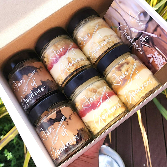gift box of six small jars filled with layers of cake, frosting and sauce
